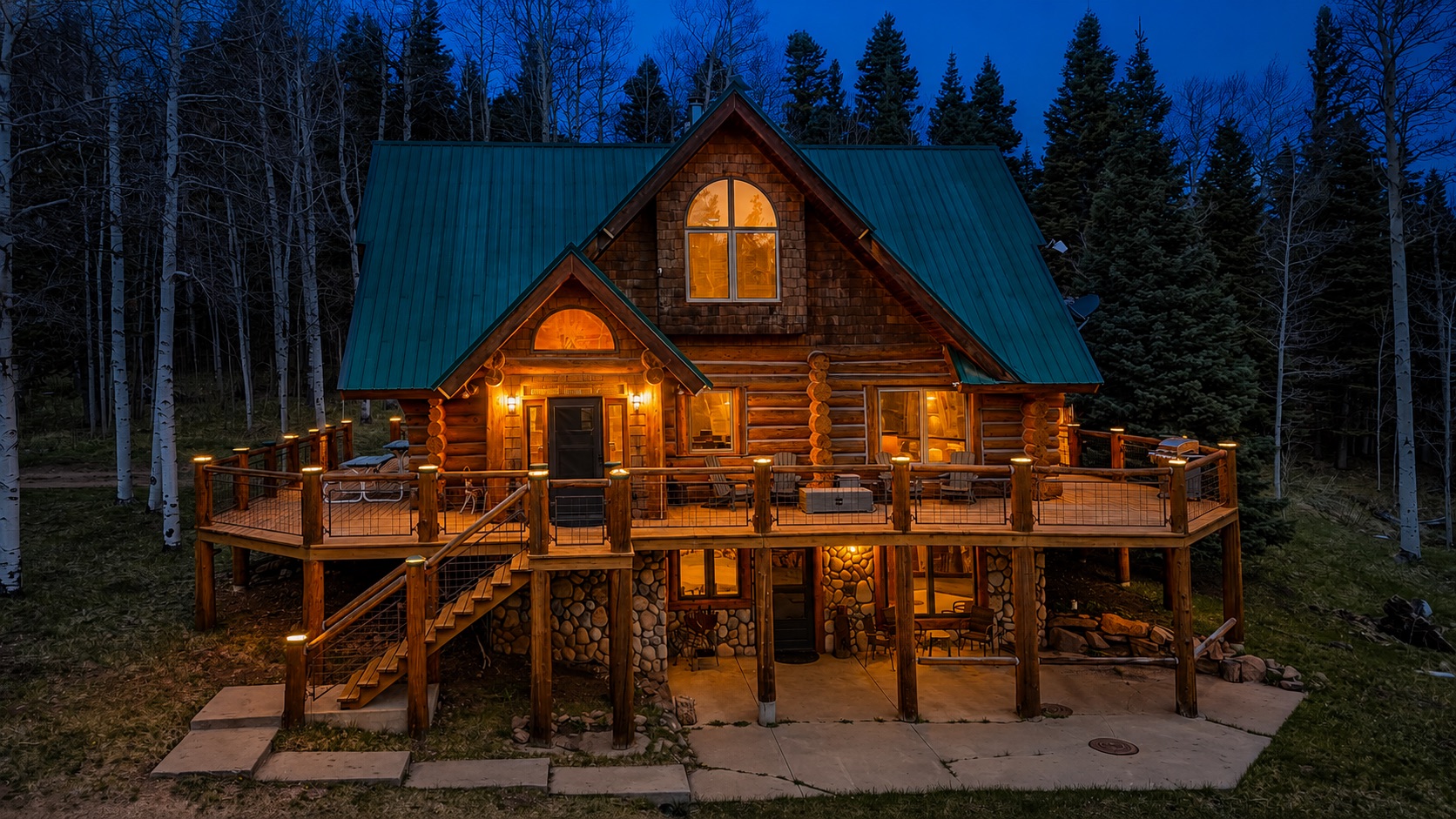 Luxury Colorado log cabin at night with warm lights and aspen trees